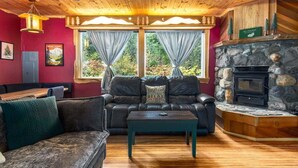 A cozy cabin interior with a stone fireplace, leather sofa, and a wooden ceiling. - Fir Tree Cabin | Grill, Fireplace (Packwood)