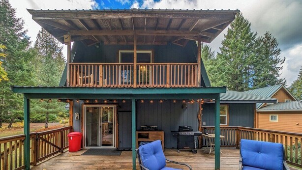 A wooden deck with two blue chairs, a barbecue grill, and a covered porch. - Fir Tree Cabin | Grill, Fireplace (Packwood)