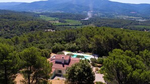 En villa med en swimmingpool, omgiven av tät skog och med berg i bakgrunden.