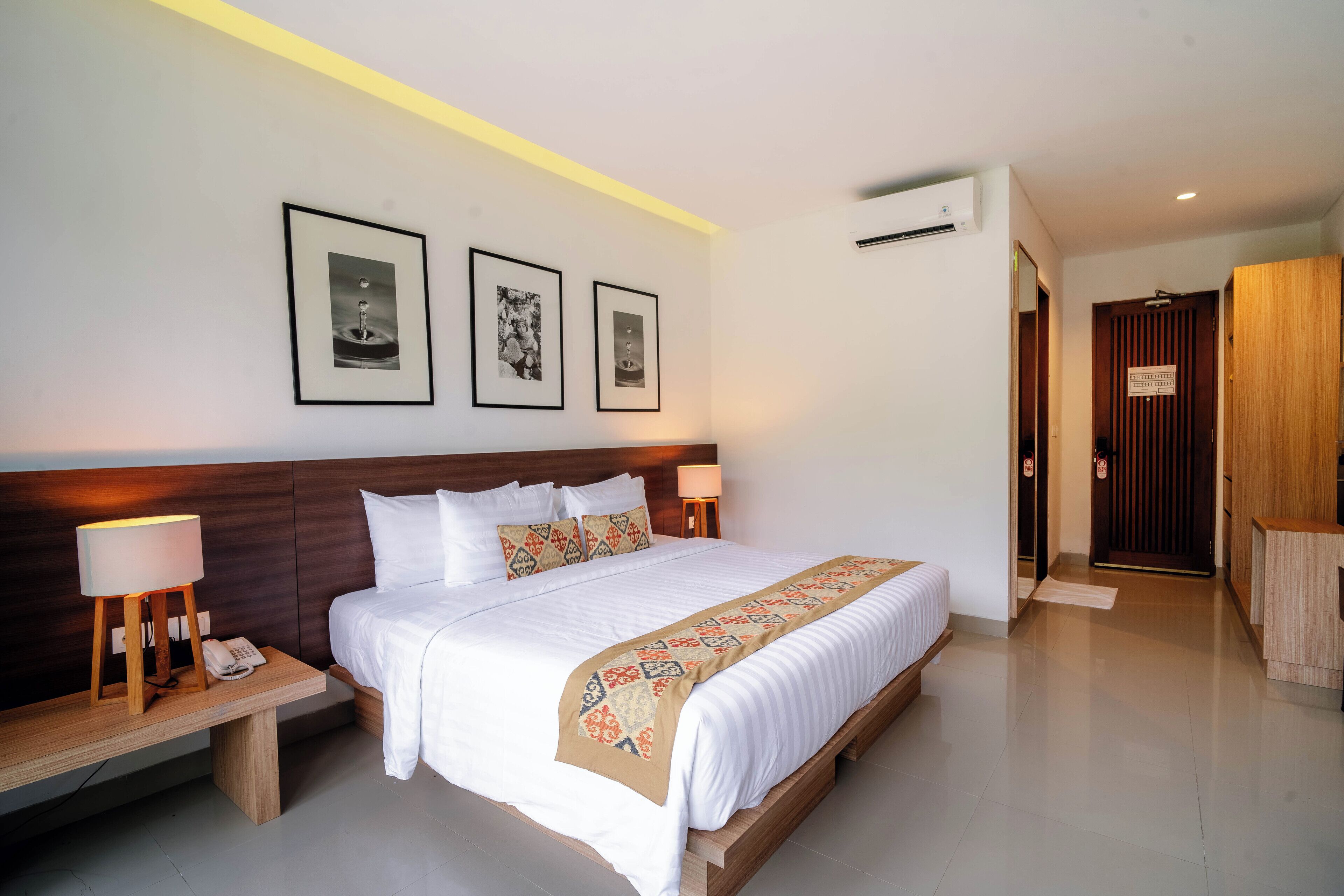 Habitación de hotel con una cama grande, lámparas de noche, teléfono en la mesita, cuadros en la pared y un armario de madera.