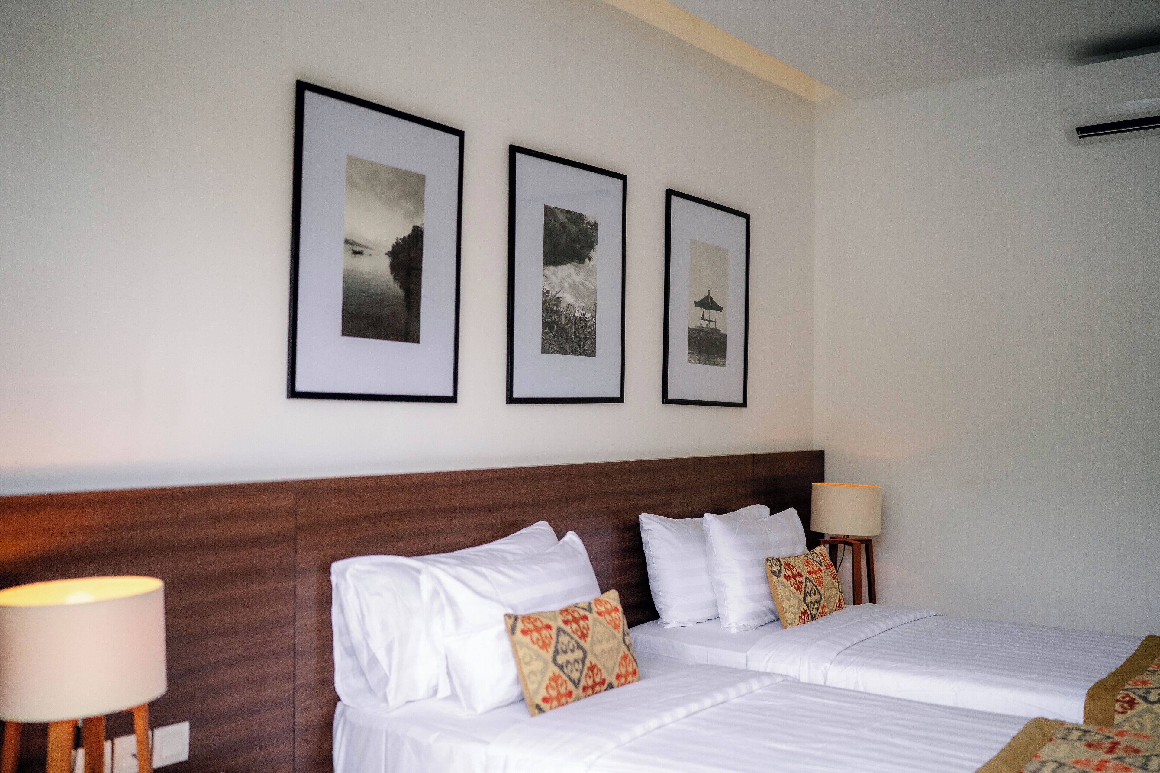 Une chambre d’hôtel avec deux lits, une tête de lit en bois, des tableaux encadrés au mur et des lampes de chevet.