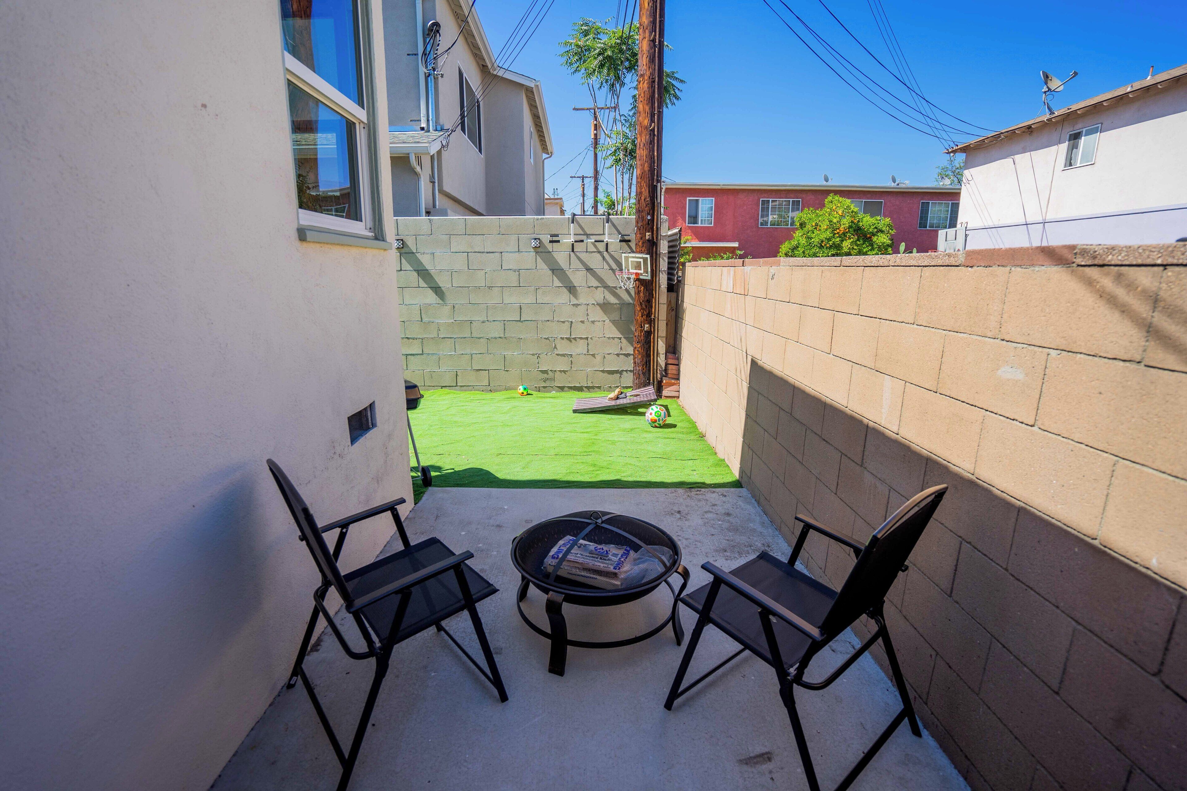 A patio area with two black chairs and a round table, a small green lawn, and a brick wall.