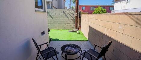 A patio area with two black chairs and a round table, a small green lawn, and a brick wall.