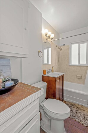 A bathroom with a white toilet, a vanity with a sink, a mirror, and a shower area with a towel rack. - Historic Quiet Home W/Free Parking by Hollywood (Burbank)