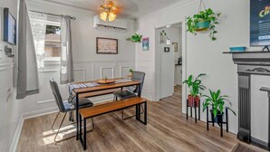 Ein Essbereich mit einem Holztisch, Stühlen und einer Bank. Üppige Topfpflanzen stehen auf Ablagen, und über dem Tisch hängt ein Deckenventilator.