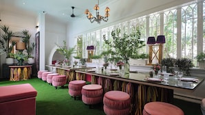 A spacious room with a long bar, green carpet, and multiple pink ottomans. - ThaoDien Boutique Hotel (Ho Chi Minh City)