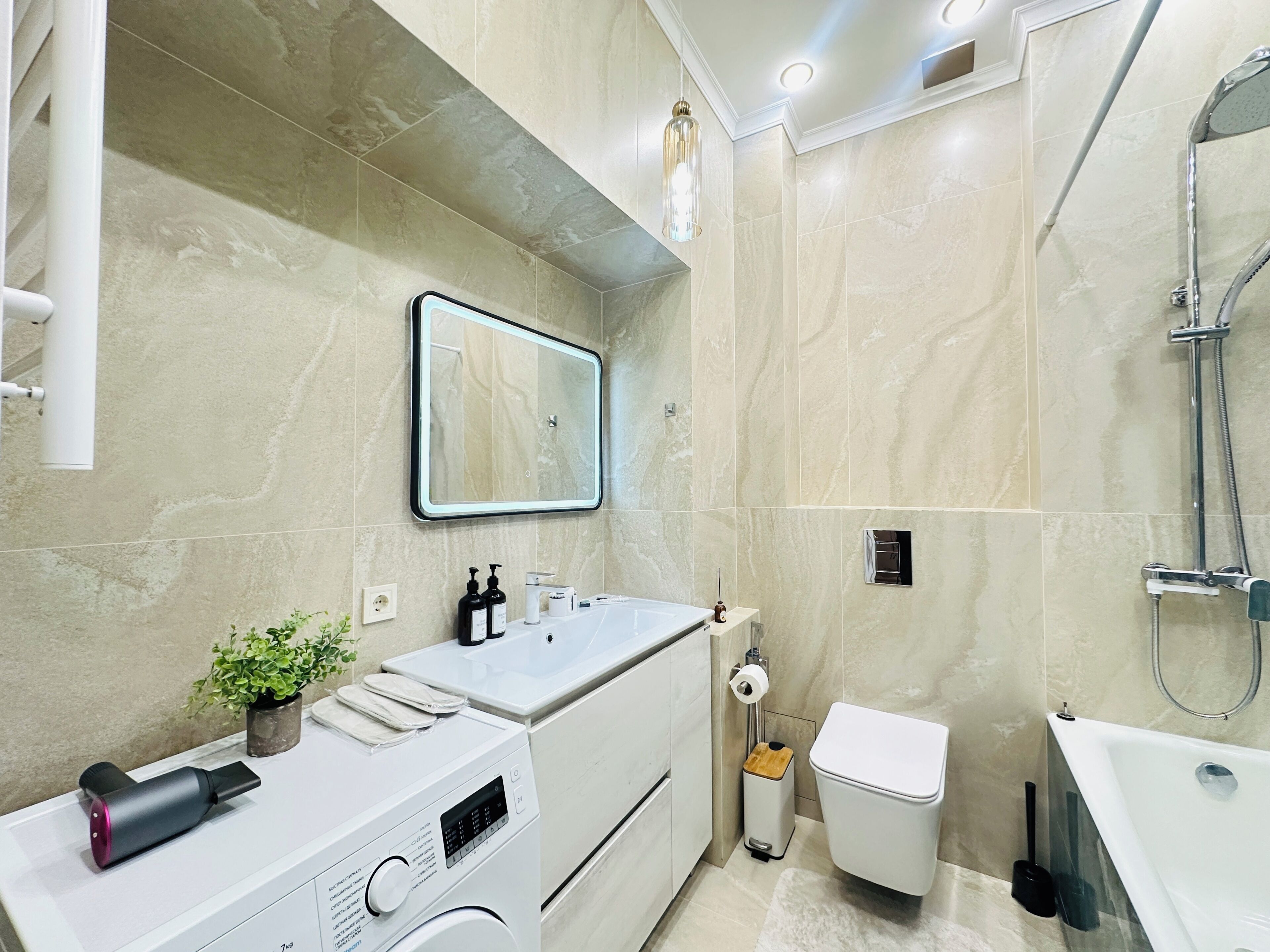 A modern bathroom with a built-in washing machine, a toilet, a shower area, and a mirror.
