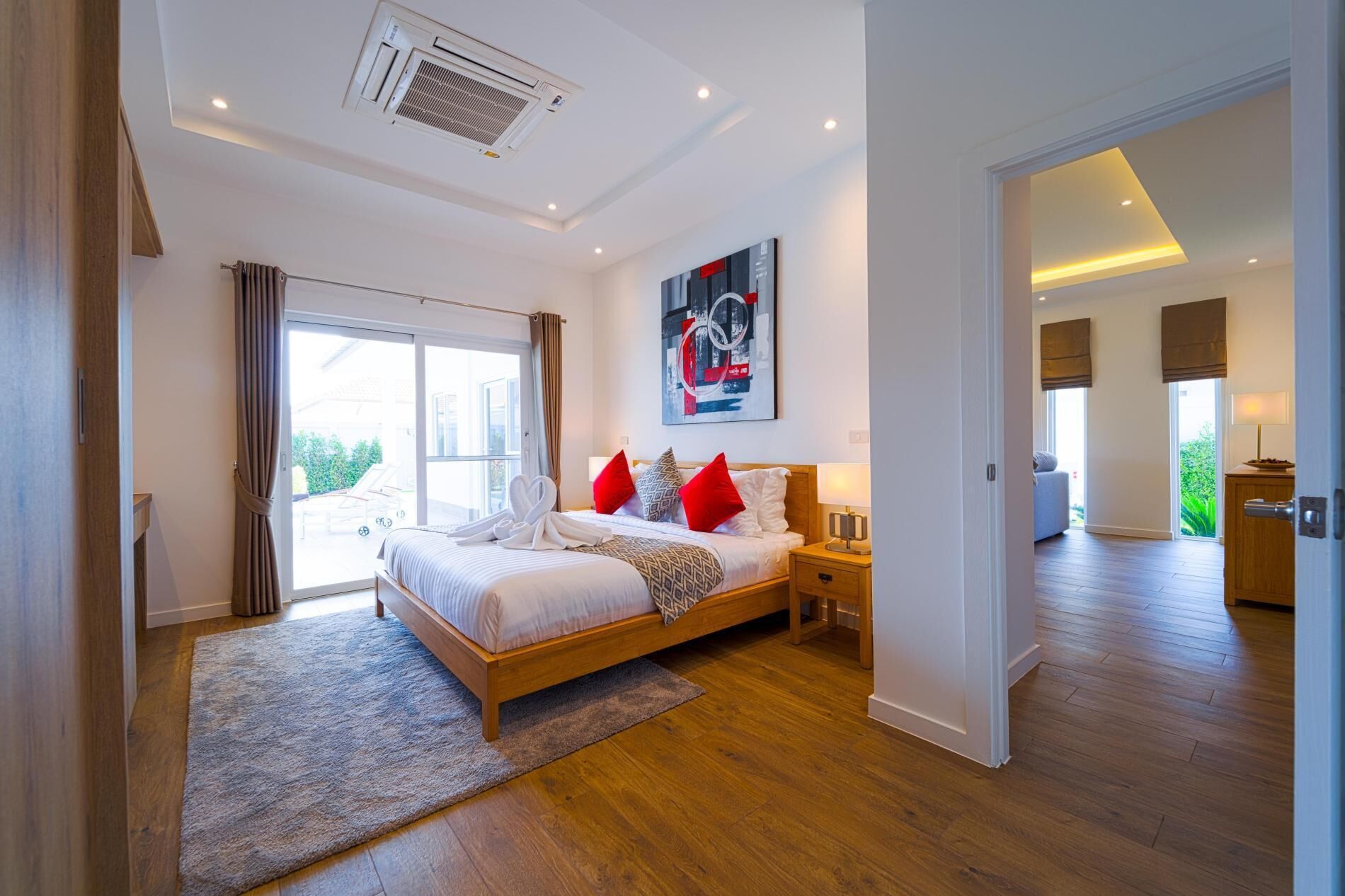 A modern hotel room with a large bed, a painting, and a view of the outdoors.
