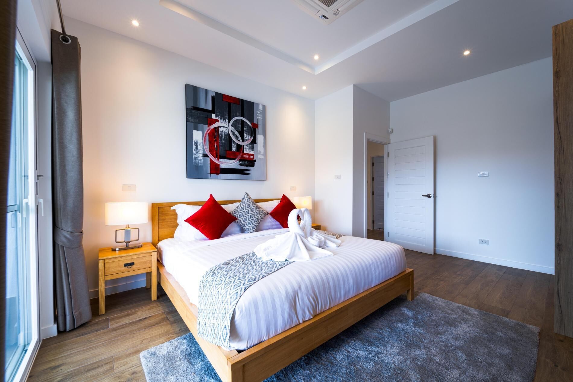 Een moderne slaapkamer met een houten bed, een groot abstract schilderij en een zichtbare deur.