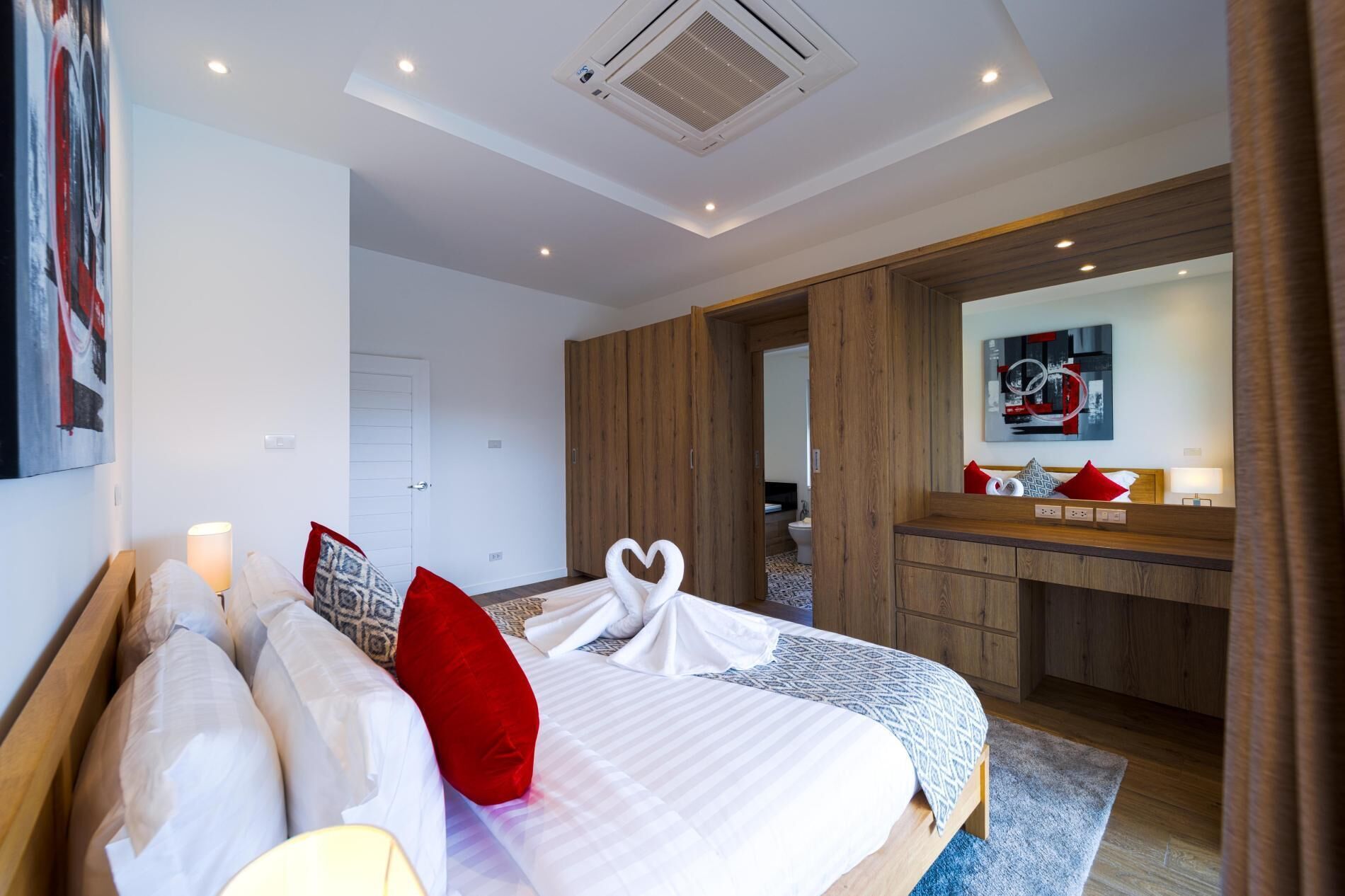 A modern hotel room with a large bed, a wooden wardrobe, a bathroom visible through an open door, and a ceiling with recessed lighting.