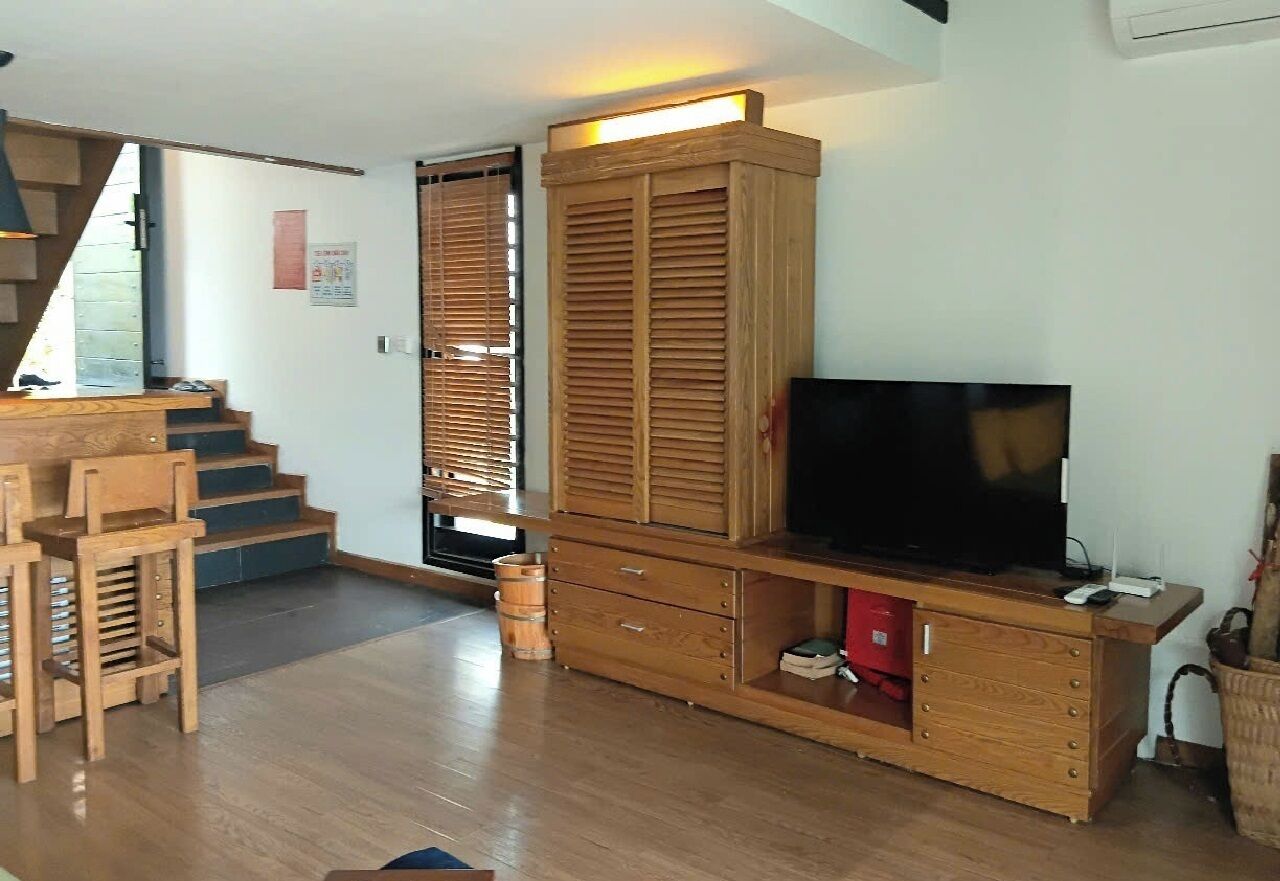 A living room with a wooden entertainment unit, a television, and a staircase leading to another level.
