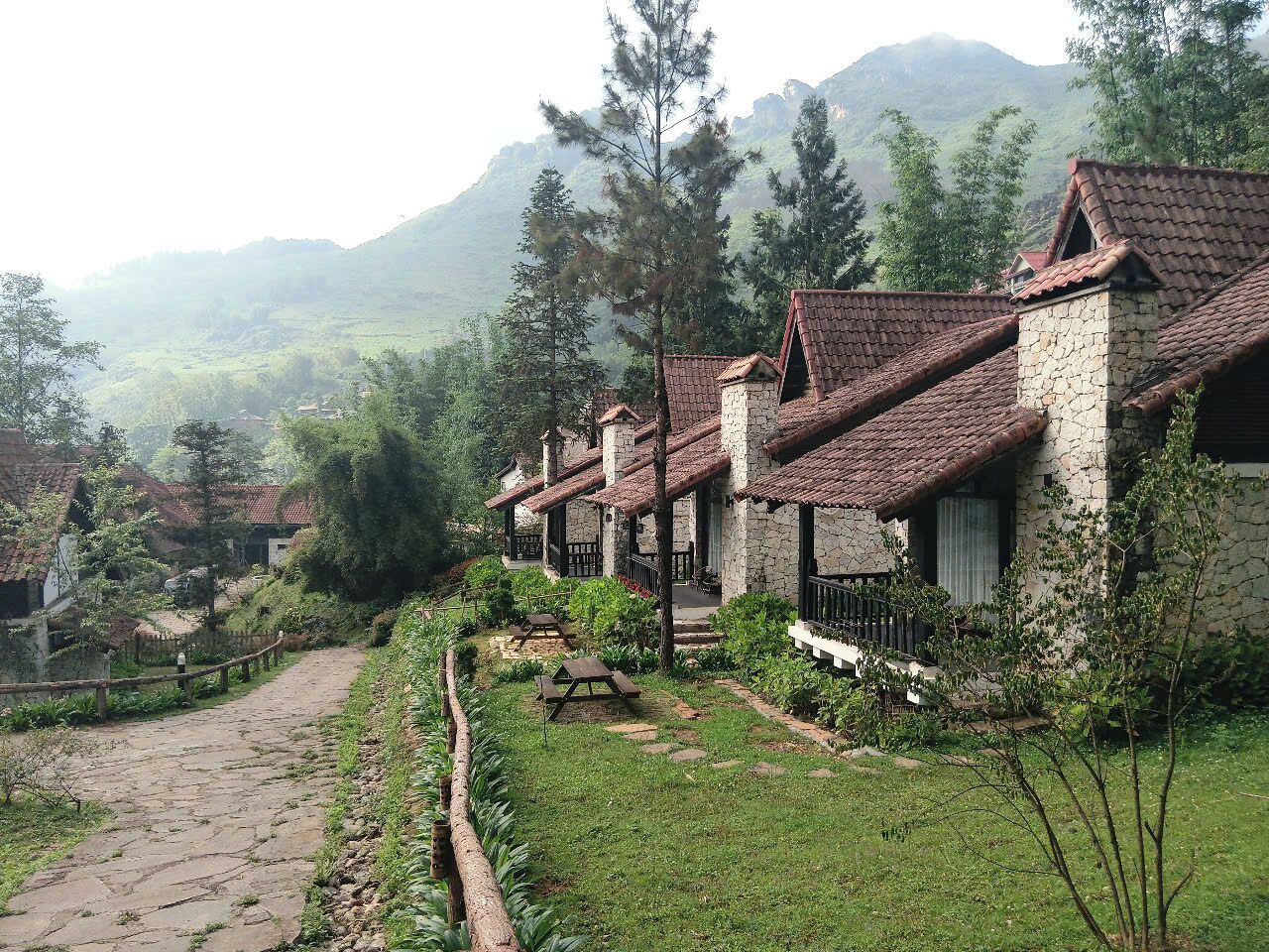 A row of stone houses with tiled roofs, a stone pathway, and a grassy area with picnic tables.