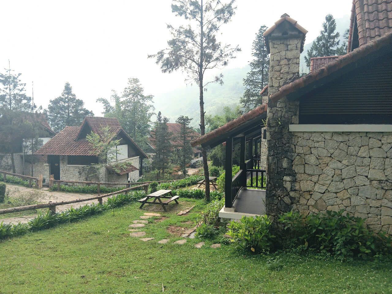 A rustic building with stone walls and a wooden roof, surrounded by a well-maintained garden with a picnic table.