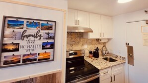 Une cuisine avec des armoires blanches, un comptoir en granit, une cuisinière en acier inoxydable et un tableau encadré accroché au mur.