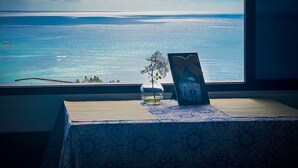 Une vue sur l’océan, prise depuis une fenêtre, avec un vase de fleurs et un tableau encadré posés sur une table.