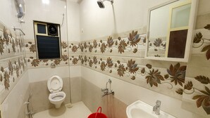A bathroom with a toilet, shower, sink, and a red bucket. - Beach Aura by Lavika Stays (Alibag)