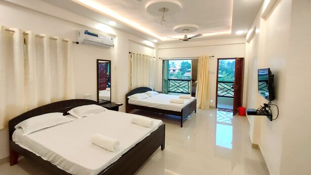 A hotel room with two beds, a ceiling fan, an air conditioning unit, a TV, and a balcony with curtains. - Beach Aura by Lavika Stays (Alibag)