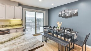 A modern kitchen with a marble countertop, a dining area with a bench, and a sliding glass door leading to a balcony. - Mountain-View Retreat w/ Hot Tub in Centerville! (Centerville)