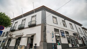Un edificio bianco con numerose finestre e balconi, una vetrina con un cartello e una strada acciottolata.