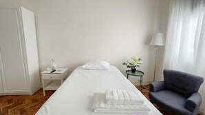 Una camera d'albergo con un letto, una sedia, un comodino, una lampada e un tavolino con una pianta.