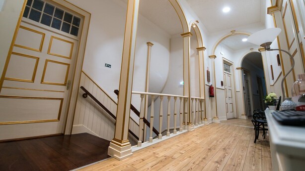 Un'ampia sala con pavimento in legno, pareti bianche e finiture dorate.