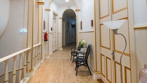 Un corridoio con pavimento in legno, pareti bianche con decorazioni dorate e una sala da pranzo con tavolo e sedie.