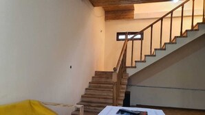 Une pièce avec un escalier en bois, un canapé jaune et une table blanche couverte de papiers.
