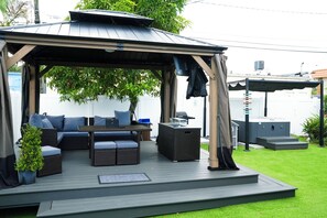 Une terrasse extérieure dotée d’un espace salon couvert, d’une petite table et d’une plante en pot.