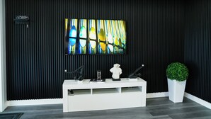 Een modern interieur met een zwart textuurmuur, een hangende televisie, een witte console tafel met decoratieve objecten, en een potplant.