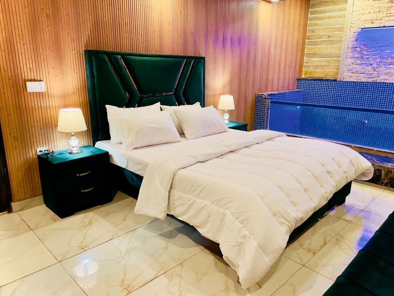 A hotel room with a large bed, two bedside tables with lamps, a wooden wall paneling, and a view of a pool.