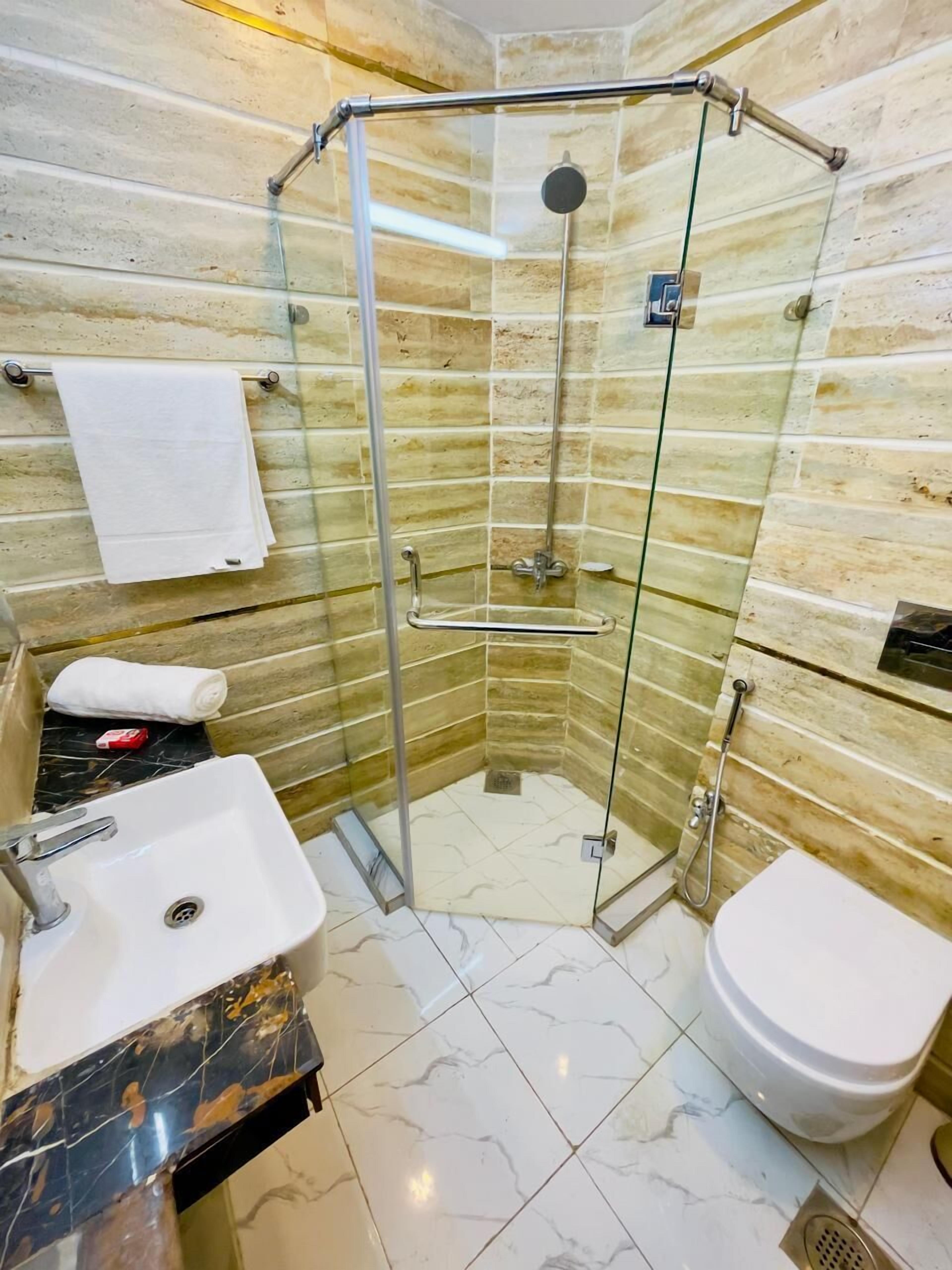 Casa de banho de canto com cabine de duche em vidro, lavatório, sanita e suporte para toalhas.