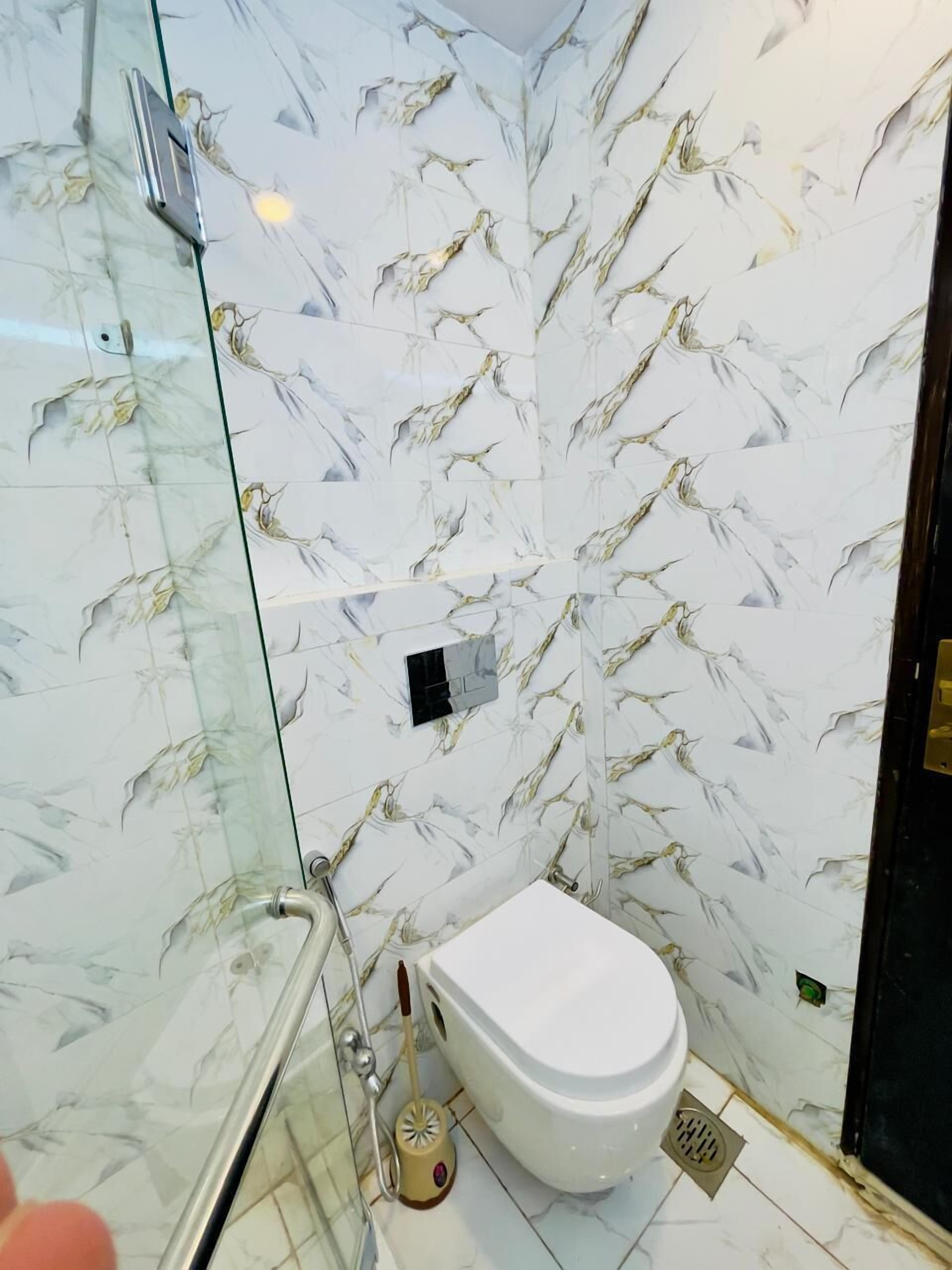 Une salle de bain comprenant des toilettes, une douche à parois de verre et un mur décoré d’un motif imitant le marbre.