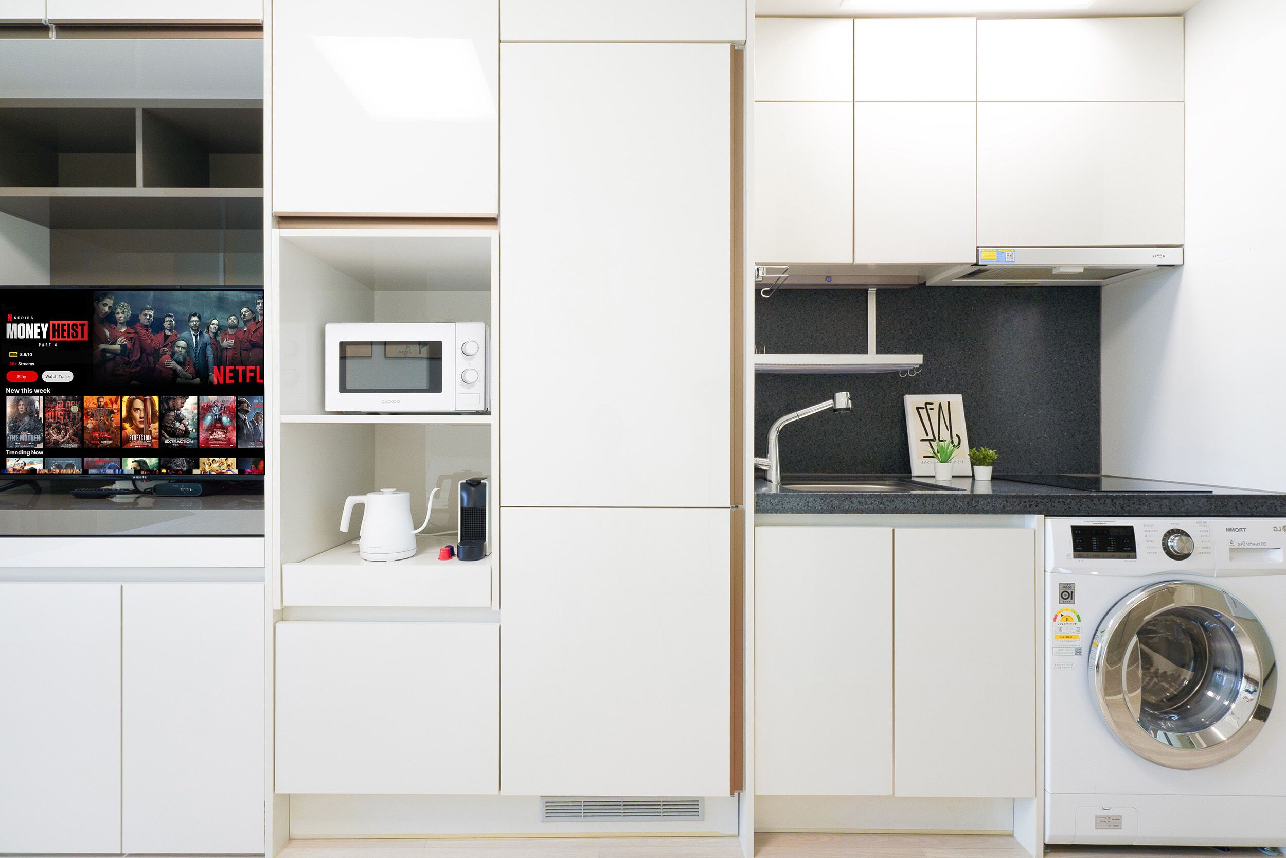 A compact kitchen with a microwave, kettle, and washing machine, and a TV displaying a Netflix interface.