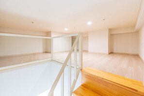 Une pièce vide avec un plancher en bois, une rambarde en verre et un escalier.