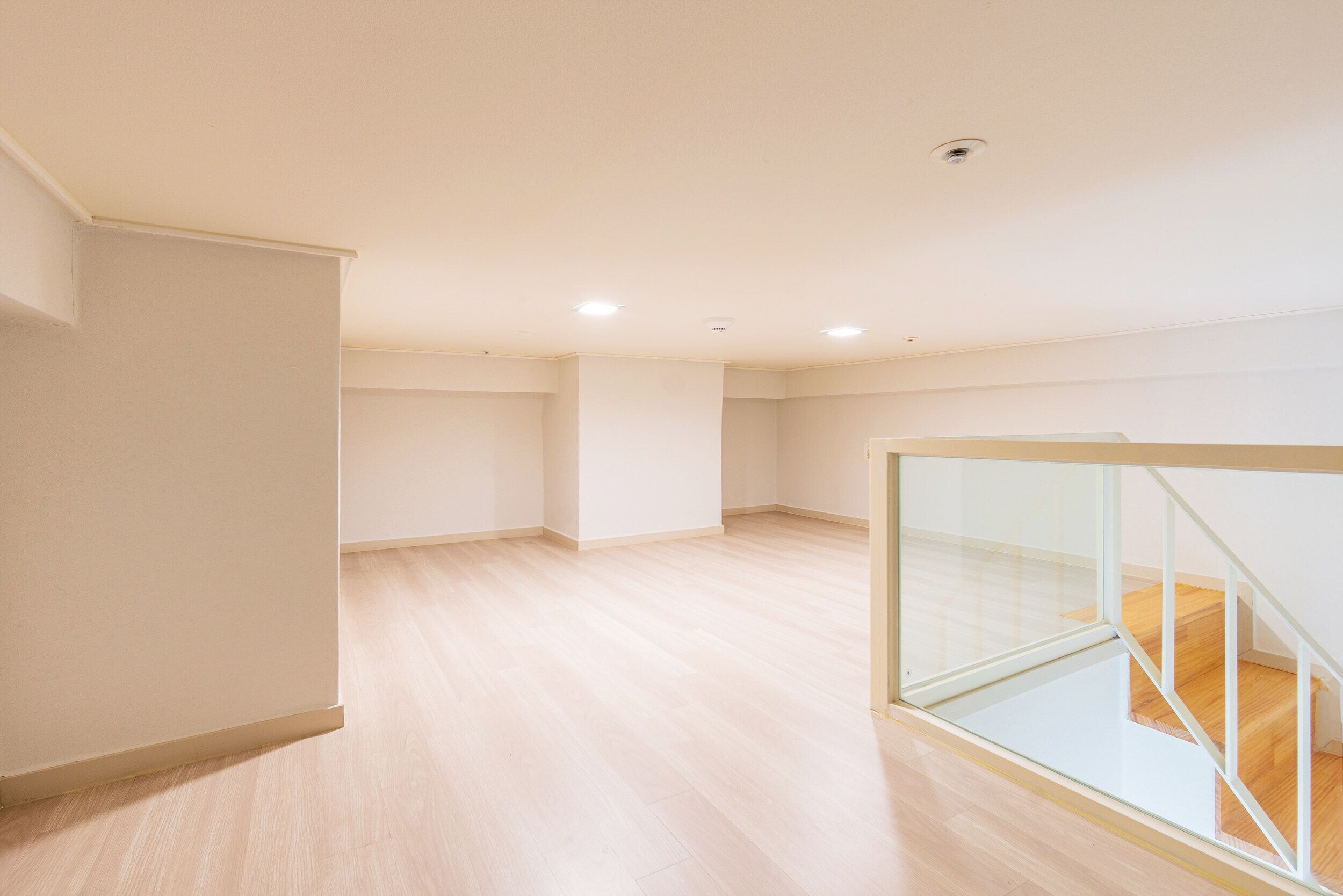 A spacious room with a wooden floor, a glass railing, and a staircase.