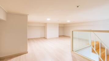 A spacious room with a wooden floor, a glass railing, and a staircase.