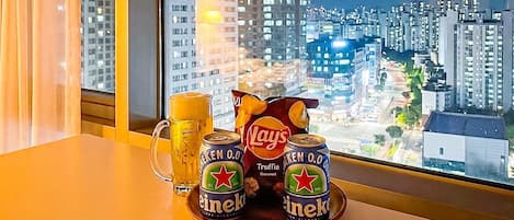 Una mesa con un vaso de cerveza, dos latas de Heineken y una bolsa de papas Lay's.