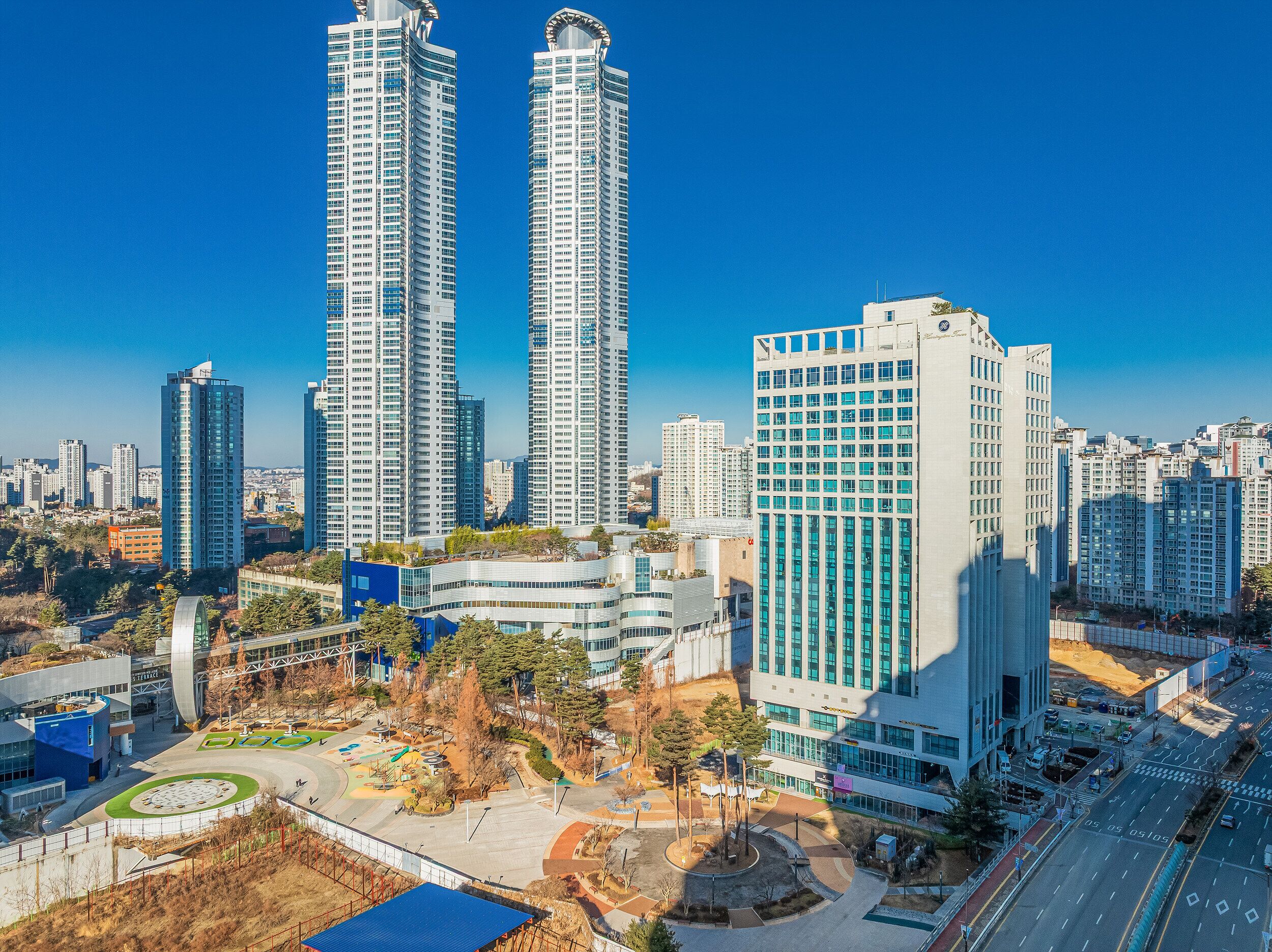 Un ensemble immobilier composé d’immeubles de grande hauteur, dont plusieurs gratte-ciel, une place centrale agrémentée d’arbres et un design architectural moderne.