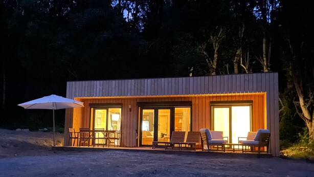Een moderne cabin met grote glazen deuren, buitenmeubels en een patio parasol.