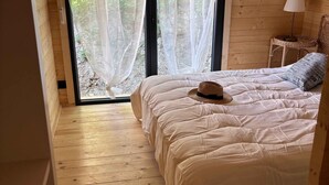 Een houten kamer met een bed, een raam met dunne gordijnen en een lamp op een nachtkastje.