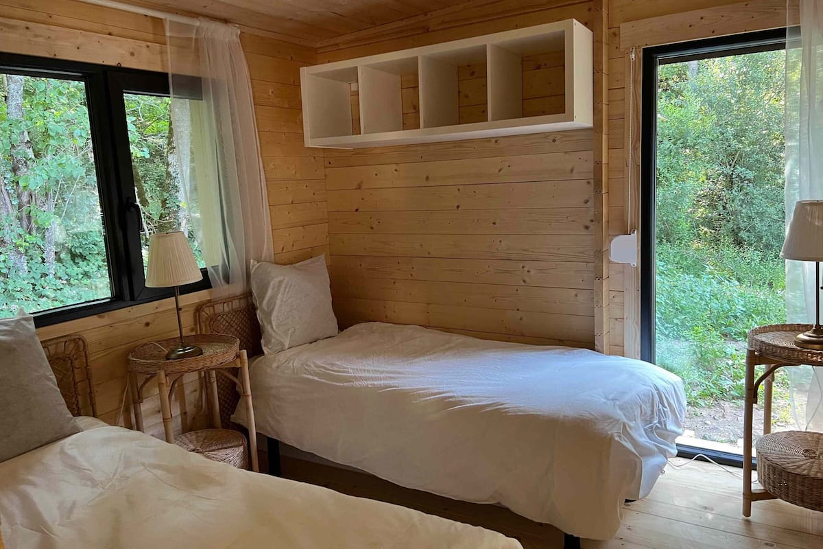 Une chambre dans un chalet en bois, avec deux lits, une petite table et une fenêtre donnant sur un paysage verdoyant.