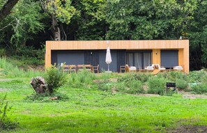 Un edificio moderno con fachada de madera, un área de estar exterior cubierta con mesas y sillas, y un gran portón de garaje.
