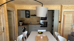 Een moderne keuken met houten wanden en een centraal eiland. Er staat een eettafel met stoelen, een schaal fruit en een kaars.