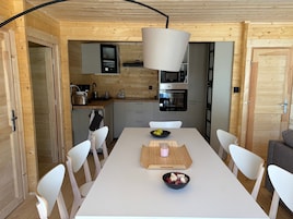Una cocina moderna con paredes de madera y una isla central. Hay una mesa de comedor con sillas, un cuenco de fruta y una vela.