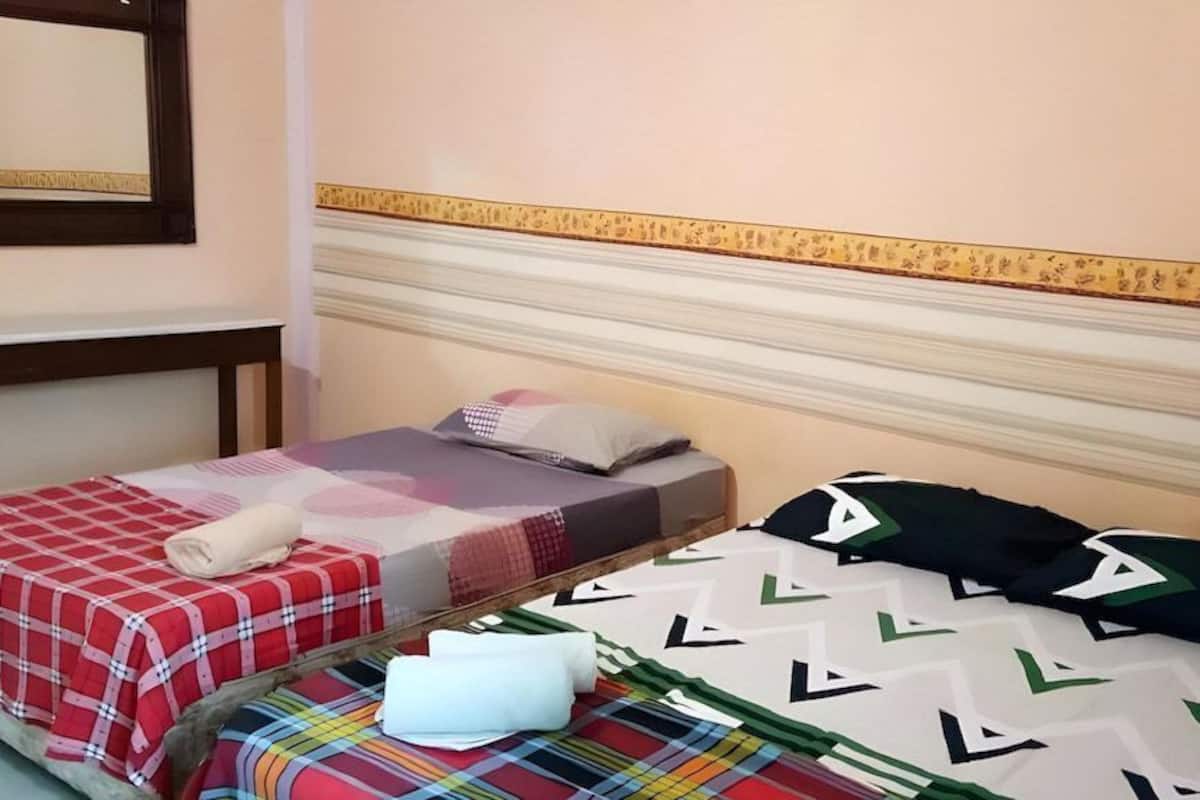 Zwei Betten mit verschiedenen Bettdecken, ein hölzernes Kopfteil und ein gerahmtes Bild an der Wand.