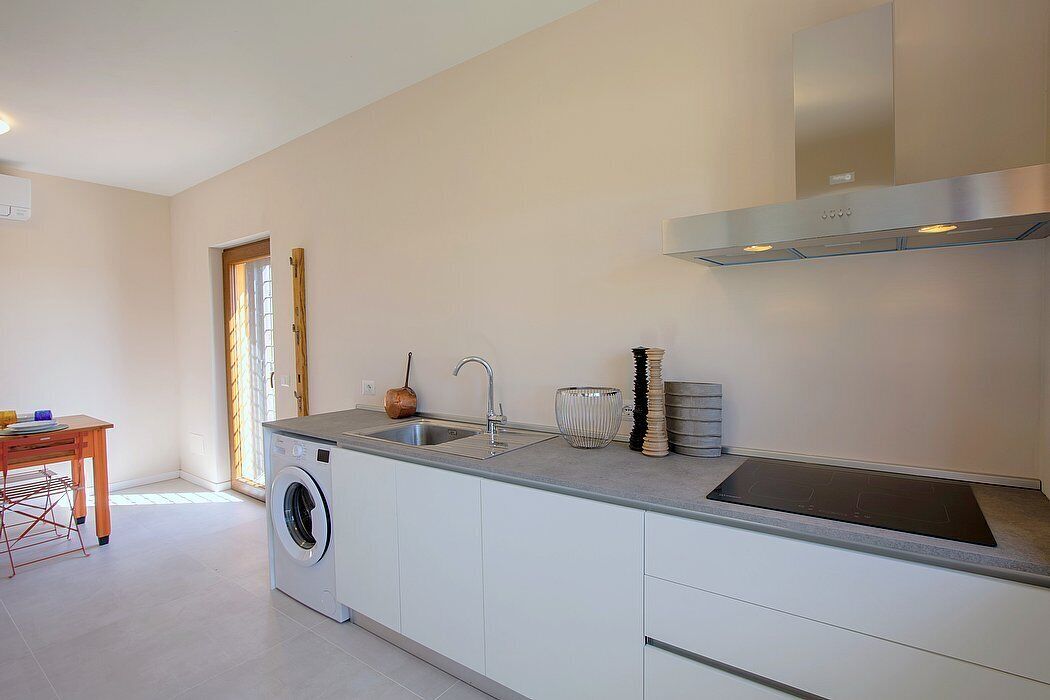 A modern kitchen with a built-in washing machine, a stainless steel range hood, and a large window.