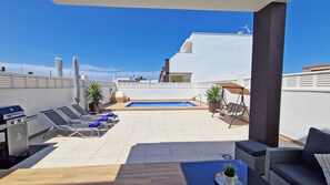 Una terrazza panoramica con piscina, lettini, barbecue e piante in vaso.