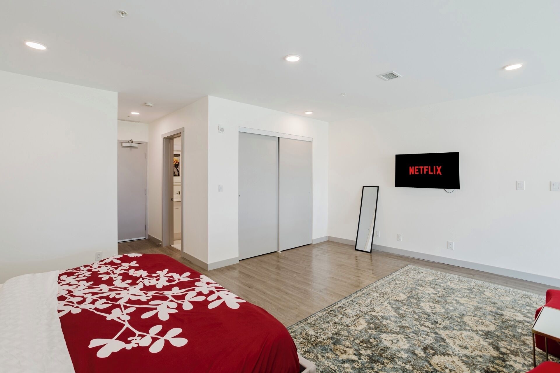 A modern hotel room with a bed, a TV, a wardrobe, and a small rug.