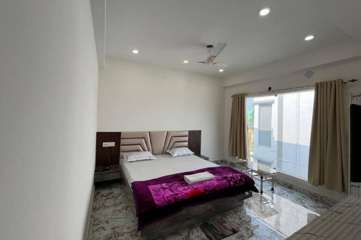 A modern hotel room with a large bed, a ceiling fan, and a large window with curtains.