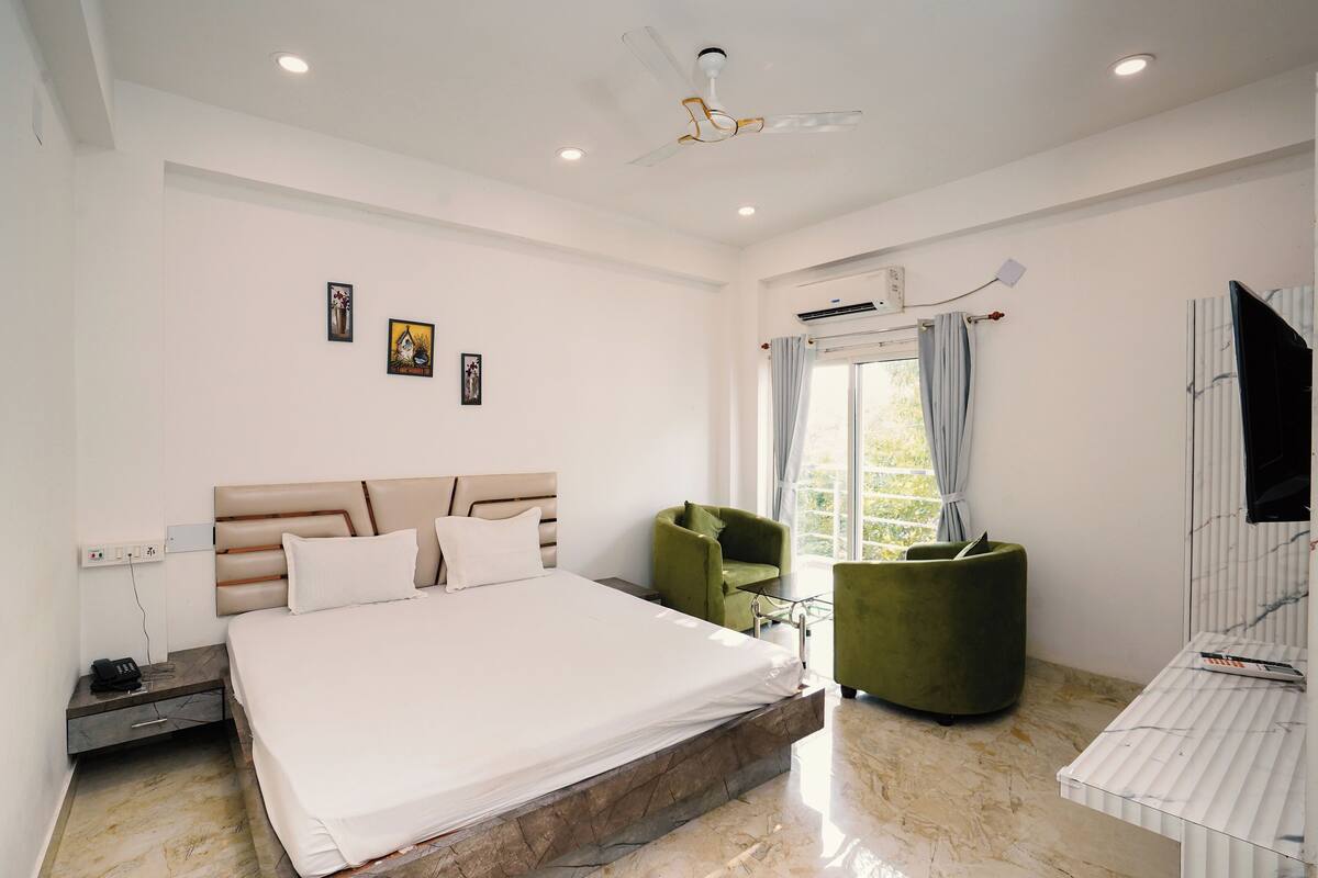 A modern bedroom with a large bed, a green armchair, a small table, and a ceiling fan.